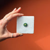 Hand holding a custom miniature painted pendant against an orange background, showing size and craftsmanship.
