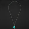 Turquoise intaglio dog necklace laid out full length on black, the bolt-ring clasp at the top and the oval turquoise pendant at the foot of the chain