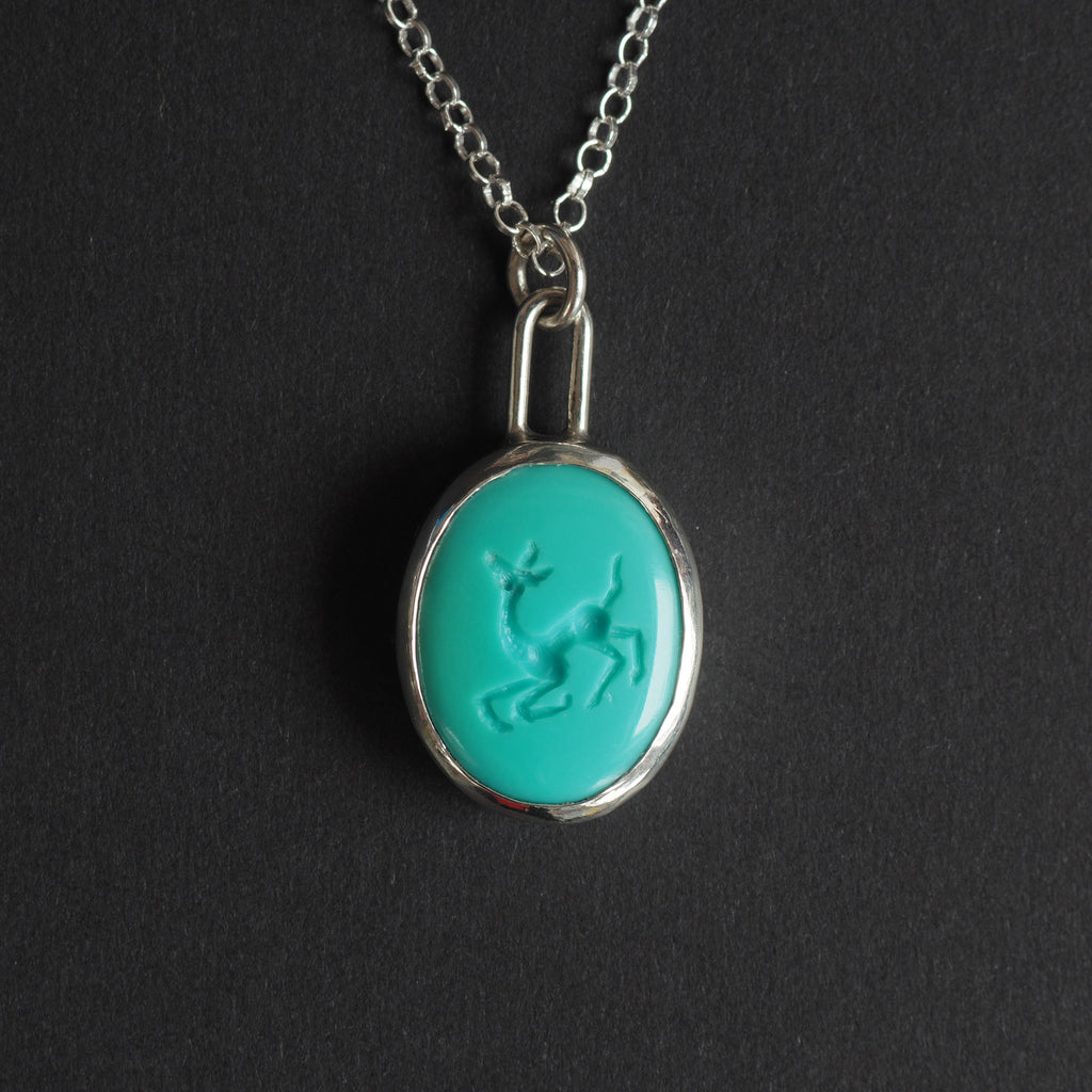 Turquoise intaglio dog necklace - a dog necklace, a long-legged dog mid-caper with its head up and its legs kicking, hand-carved into a bright turquoise oval