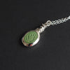 Field mouse intaglio necklace at an angle on black, the mouse leaning over the bezel's edge and the carved stems and seed heads clear in the turquoise
