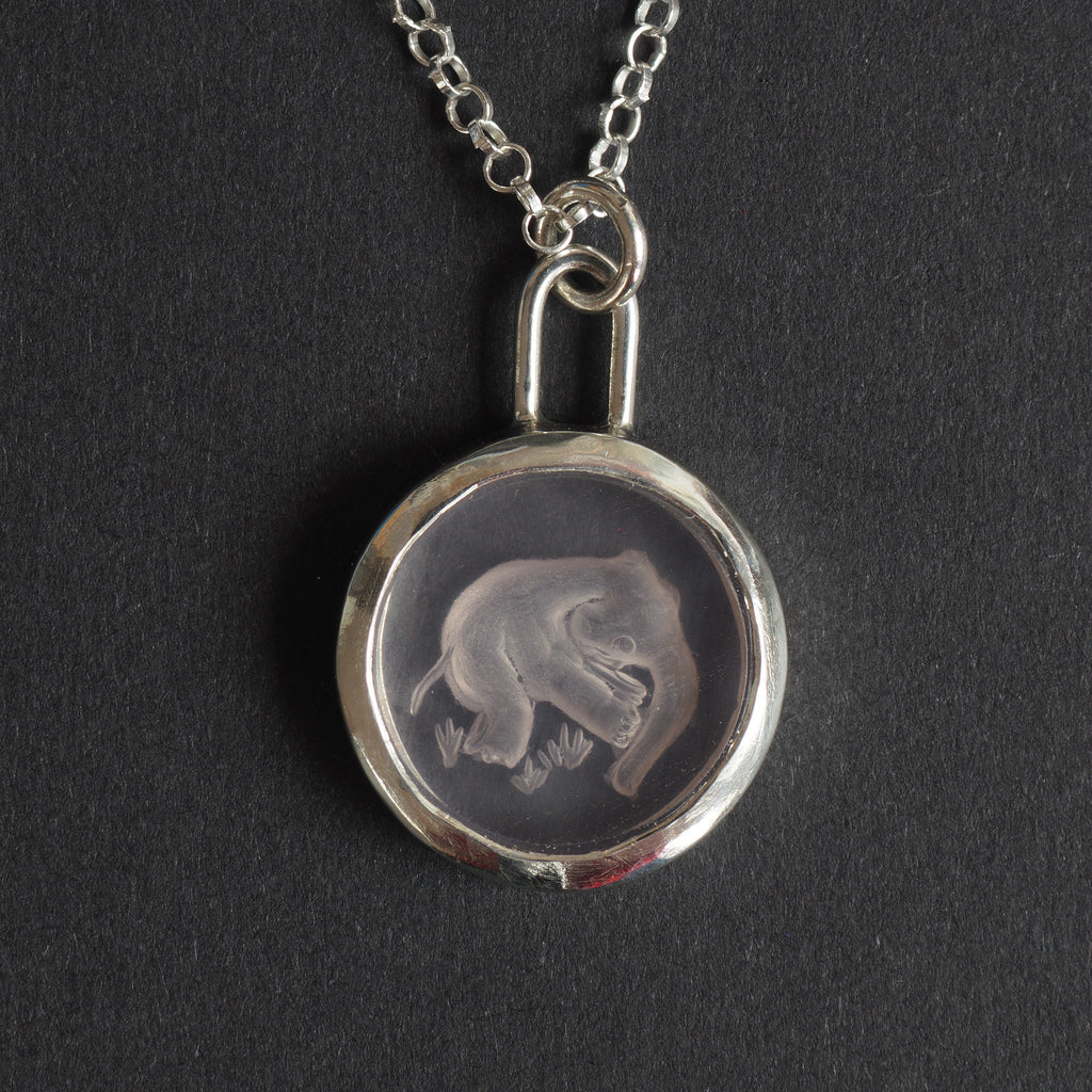 Pink Elephant reverse carved intaglio quartz necklace - an unusual necklace, an elephant caught mid-air, reverse-carved into a disc of the palest pink quartz above tufts of grass