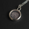 Pink Elephant reverse carved intaglio quartz necklace at an angle on black, the elephant reading pale through the clear quartz, its trunk curled and its legs tucked