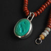 turquoise intaglio cat necklace on red jasper at an angle, the pendant in focus and the red jasper receding, the bezel bright against the turquoise