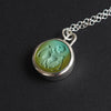 Turquoise Skeletal Torso intaglio necklace at an angle, the turquoise shading from blue to olive across the carving and the loop bale above it