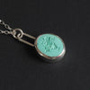 Turquoise Vase of Flowers intaglio necklace at an angle on black, the bezel's depth along the lower edge and the chain running to the upper left