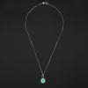 Turquoise Vase of Flowers intaglio necklace laid out full length on black, the bolt-ring clasp at the top and the oval pendant at the foot of the chain