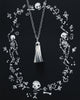 Silver ghost necklace displayed against a black illustrated background of skeletons and floral motifs by Candice Tripp.